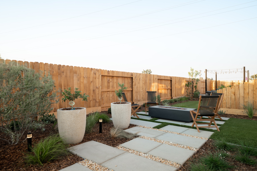 A backyard with a fence and a patio with a chair and a table.