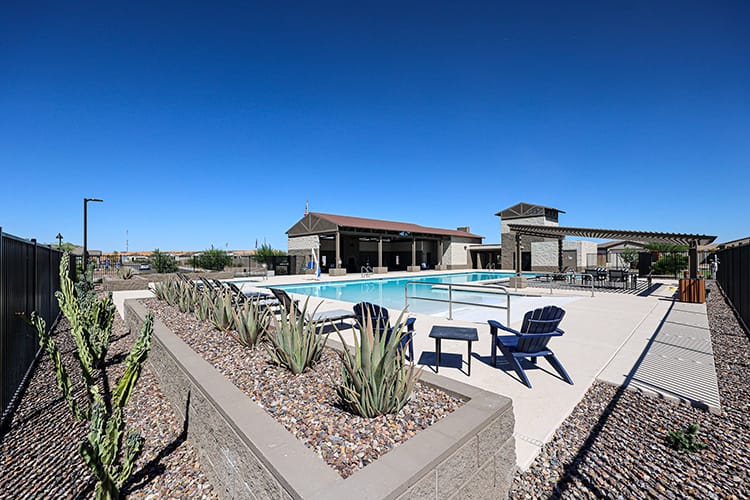 A swimming pool with a patio and chairs and a building in the background.