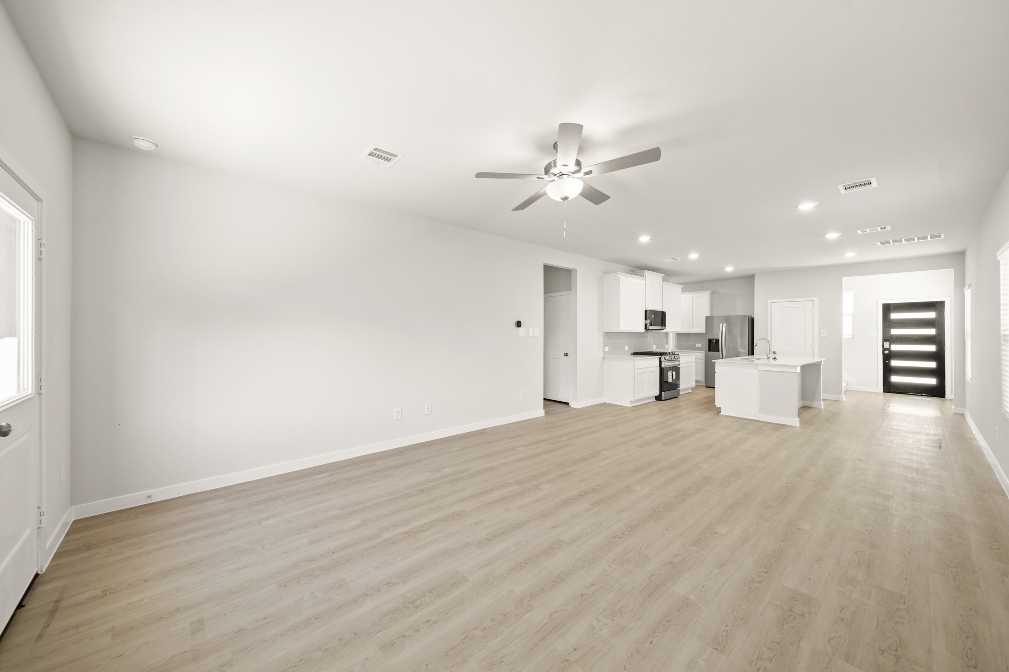 A large empty room with a ceiling fan and a wood floor.