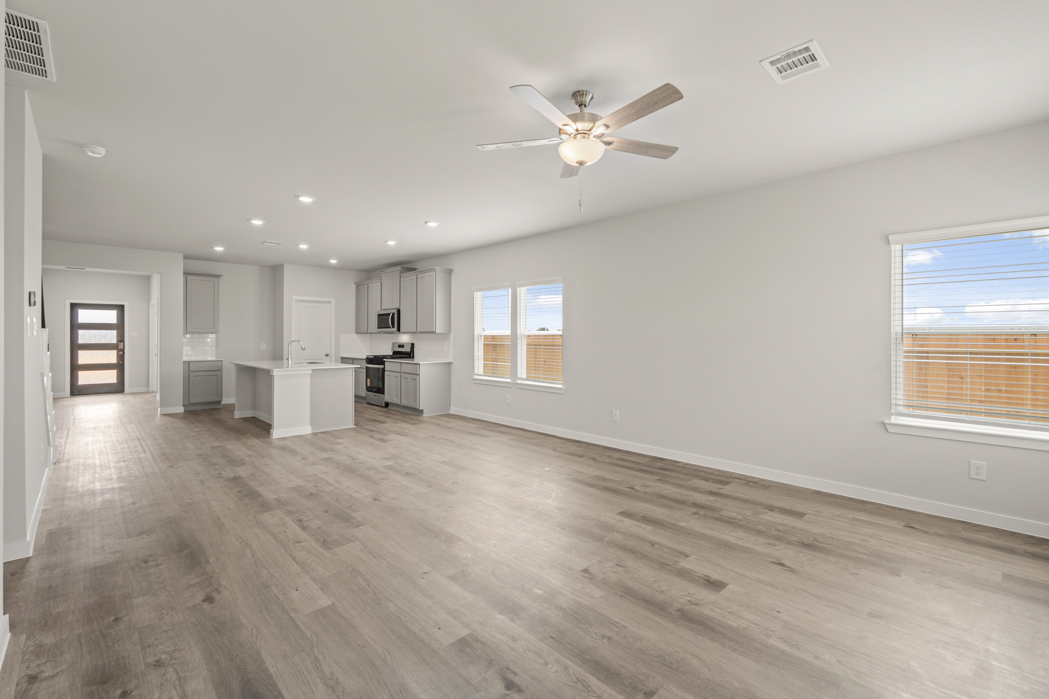 A large empty room with a ceiling fan and a wood floor.
